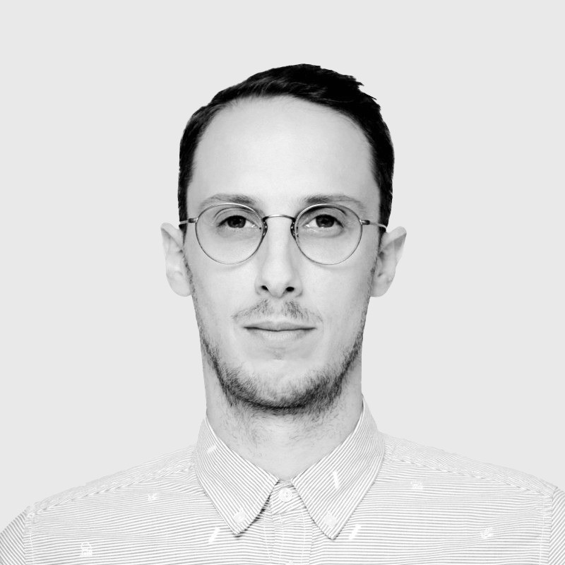 Portrait of a man with brown hair and glasses on a flat gray background.